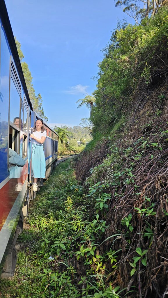 Florine hangt uit de treindeur op de treinrit van Ella naar Nuwara Eliya