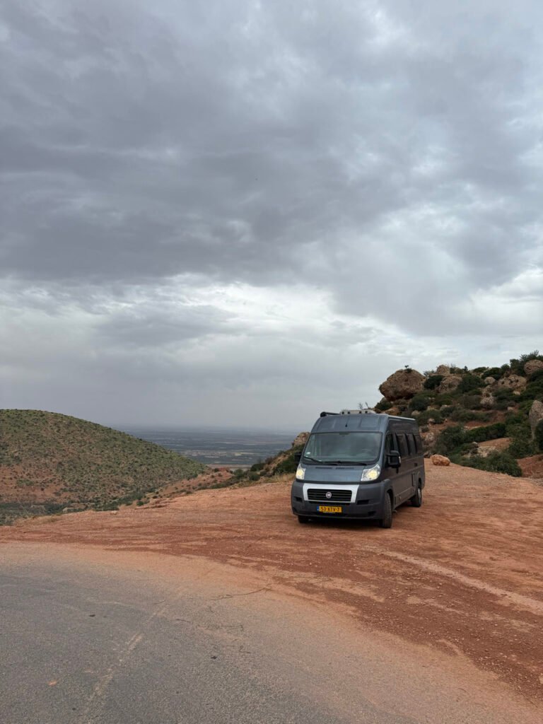 Der Camper auf einer roten Bergstraße unter bedrohlichen Wolken im Atlas
