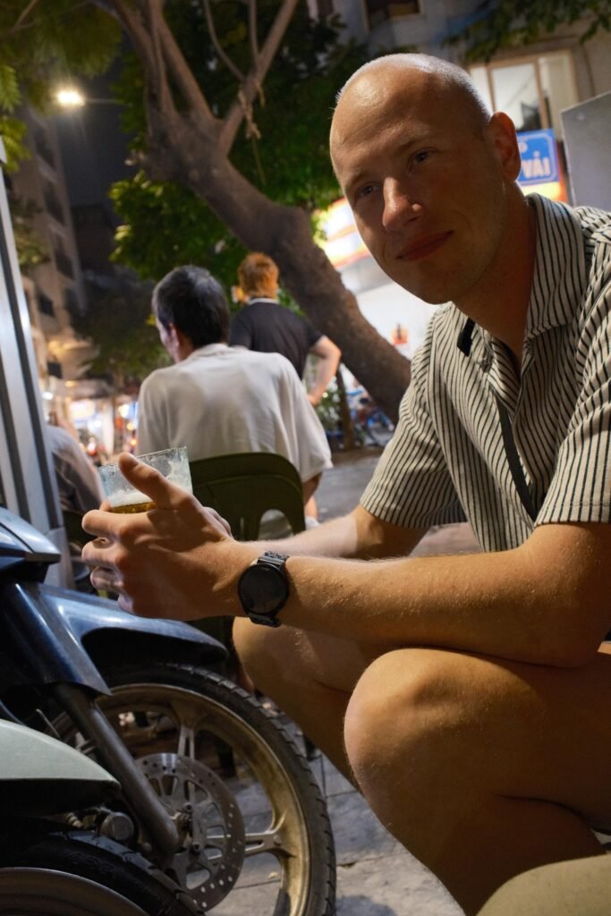 Julian met een glas bia hơi op een laag stoeltje langs de straat