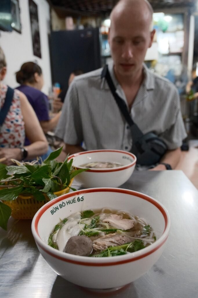 Julian aan tafel met een kom bún bò Huế voor zich