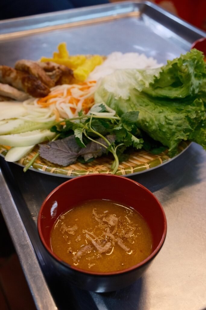Schaal met nem nướng, rijstnoedels, sla en kruiden, met een kommetje saus