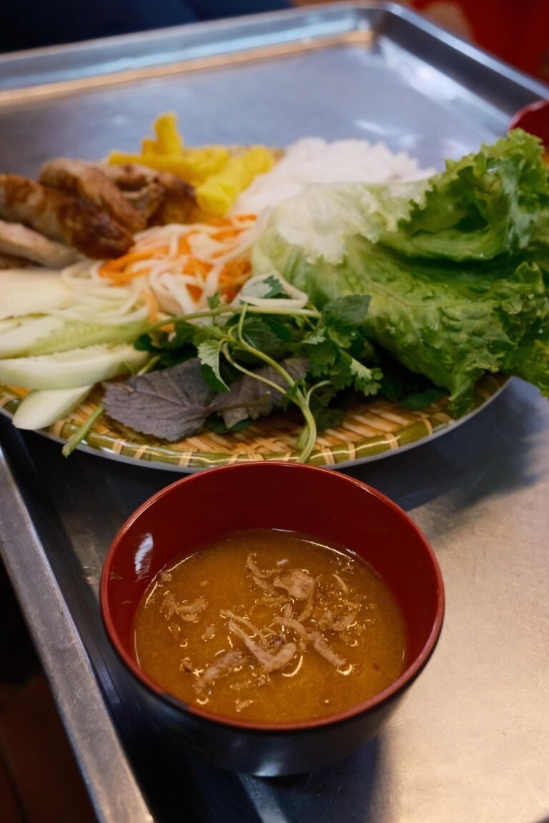 Schaal met nem nướng, rijstnoedels, sla en kruiden, met een kommetje saus